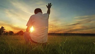El don de fe. Hombre sentado frente al sol levantando sus manos
