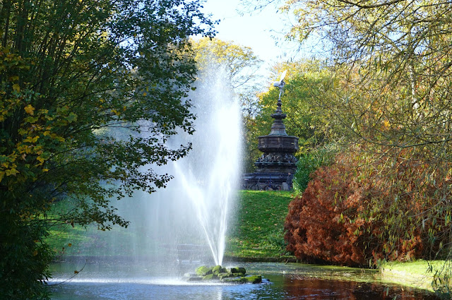 autumnal shot of the lake, statue, trees and water feature in sefton park, liverpool