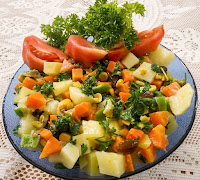 A dish of vegetables of carrots, white irish potato, celery, kale, sweet bell pepper, tomato, nuts, and rasins.