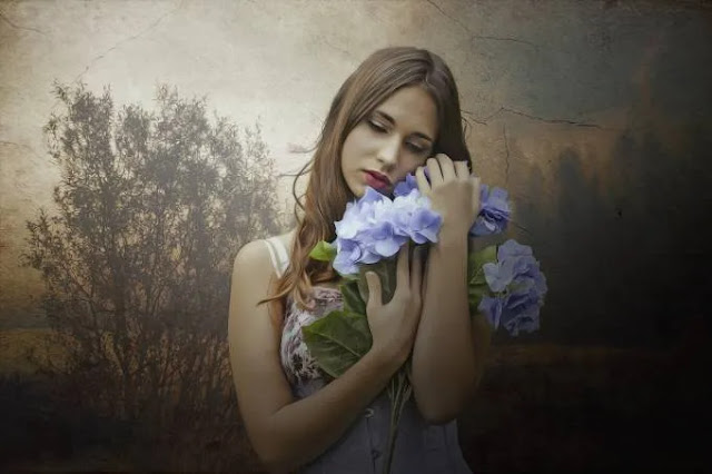 An image of a beautiful girl in white dress holding blue colored flowers- sad girl dp