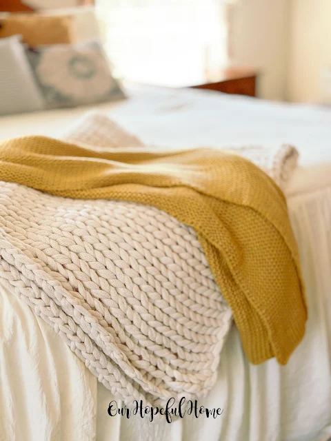 chunky knit blanket on foot of bed with golden throw blanket.