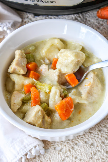 chicken and dumplings in a white bowl with a lace background and a spoon in the bowl.