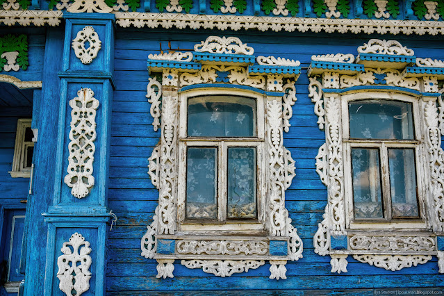 Белые резные наличники у синего, деревянного дома