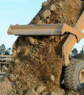 Yellow dump truck bed dumping a load of dirt.