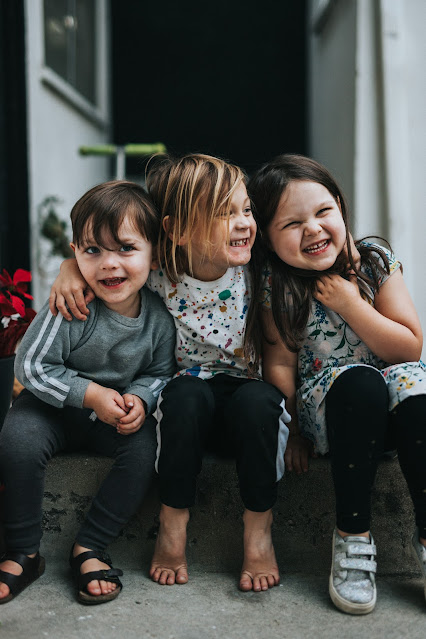 three smiling children sitting on step:Photo by Nathan Dumlao on Unsplash