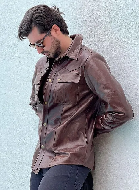 Handsome dark-haired Man 2 gazing sleeting against the wall wearing a brownish tan leather shirt and sunglasses