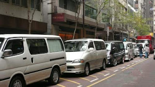 Image of a row of grey-market transport vehicles, in Hong Kong, waiting for grey-market goods to be loaded for shipments to the port.