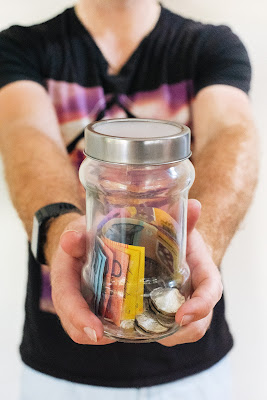 Persona sosteniendo un tarro con billetes y monedas, ofreciéndolos a la cámara