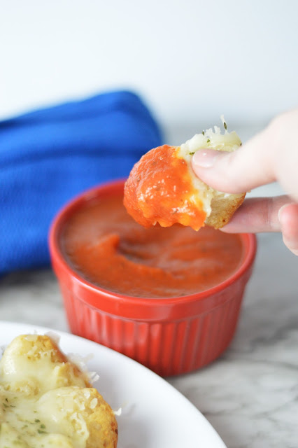 a hand dipping a piece of bread into pizza sauce.