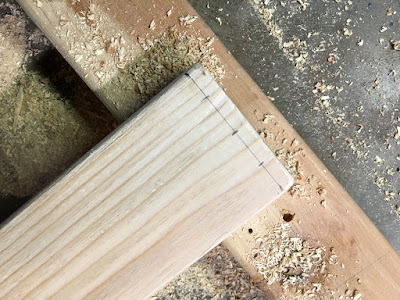 A pale board propped on another sawdusty board, with three pencil marks in a line just across the end, a bare half-inch from the end.