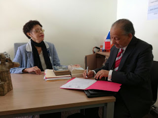 Arlene Severino (a la izquierda, sentada detrás del escritorio) observa a Huchi Lora (sentado a la derecha) en el momento en que el escritor firma la autorización para la conversión de sus obras a formatos accesibles.