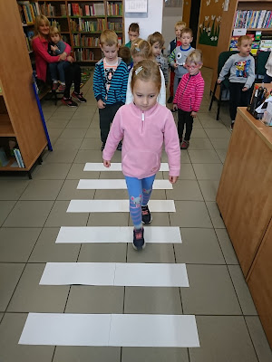 Na zdjęciu przedszkolaki przechodzą przez pasy w bibliotece