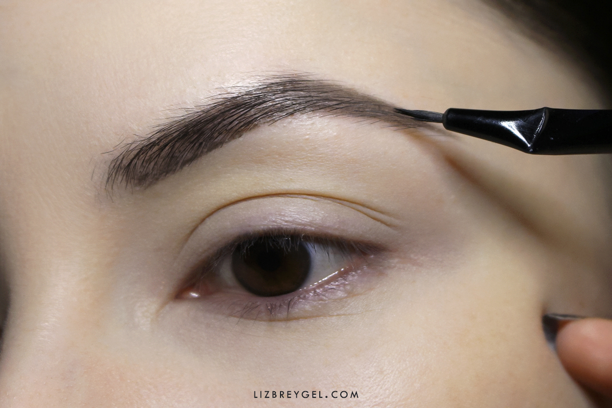 a close-up of woman's brown eye with hooded eyelid  a makeup being applied to the eyebrow