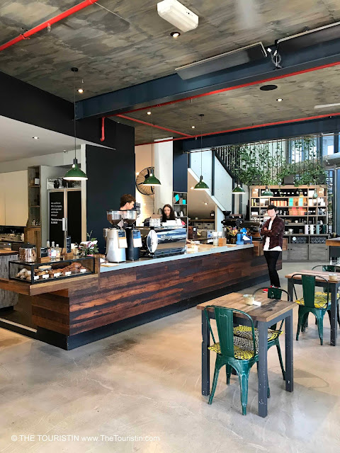 Green chairs with colourfull cushions, concrete floor and a large wooden cafe counter