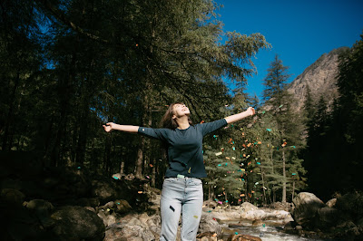 Woman stands among forest with her hands spread in joy