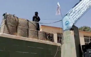 Seorang pejuang berjaga di samping bendera Taliban yang dikibarkan di gerbang di luar markas polisi, di kota Ghazni, Afghanistan dalam tangkapan layar ini diambil dari video yang dirilis oleh Taliban pada 12 Agustus 2021. Handout Taliban/via REUTERS