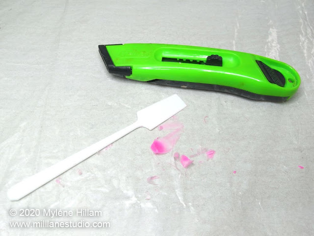 A utility knife, a cleaned plastic spatula and the cured resin that has been removed