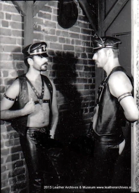 Two Leathermen flirting in black gear and Muir cap