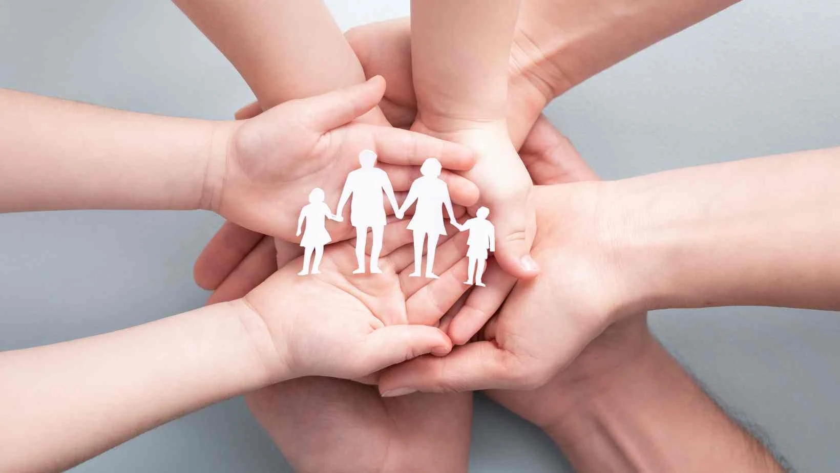 stock image showing 4 people's hands, palms up and together with a paper cut out of a family on their hands