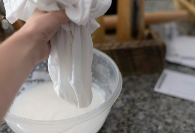 coconut milk being strained in a white flour sack towel hanging over a bowl