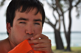 Close-up of Darrell's face which is half covered by the orange tube he is attempting to blow up