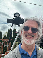 Grey haired man with a beard, digital camera aimed at the sun in the background; crescent sun on camera's LCD.