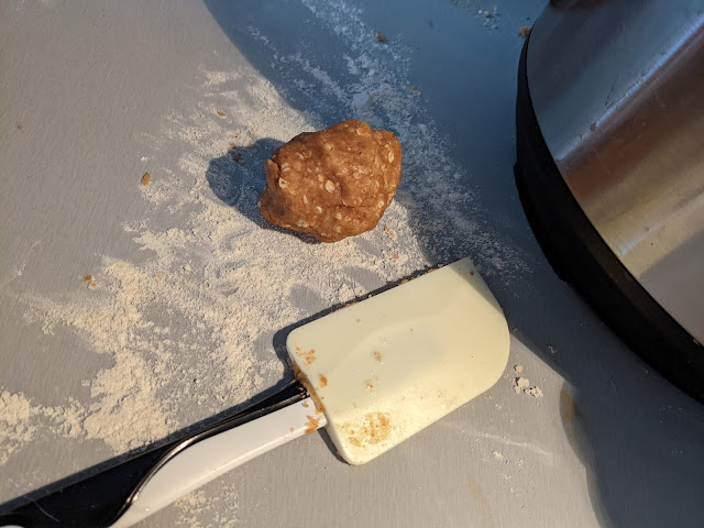 A lump of peanut butter dog biscuit dough on a gray, floured kitchen counter. A spatula next to it for scale - the lump of dough is about the size of the head of the spatula, which is a standard plastic IKEA spatula.