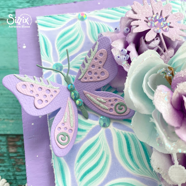 Aqua and purple mixed media panel created with Sizzix creamy matte acrylic paints, defined petals embossing folder and layered stencil, patterned butterflies die, Tim Holtz vault wildflowers die set; Prima Marketing Aquarelle Dreams flowers; Pinkfresh Studio Jewels; and lace.