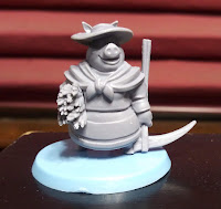 One of the player pieces. A grey plastic miniature of an anthropomorphised pig wearing a sun bonnet and scarf, holding a scythe and a bundle of straw, on a light blue base.