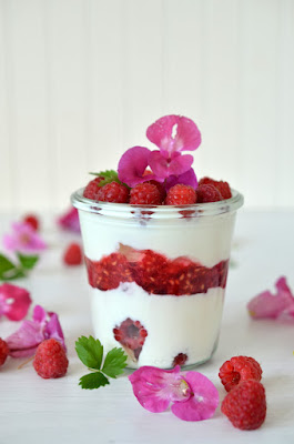 Geschichtetes Dessert aus weißer Creme und Himbeeren, dekoriert mit frischen Himbeeren und Springkrautblüten.