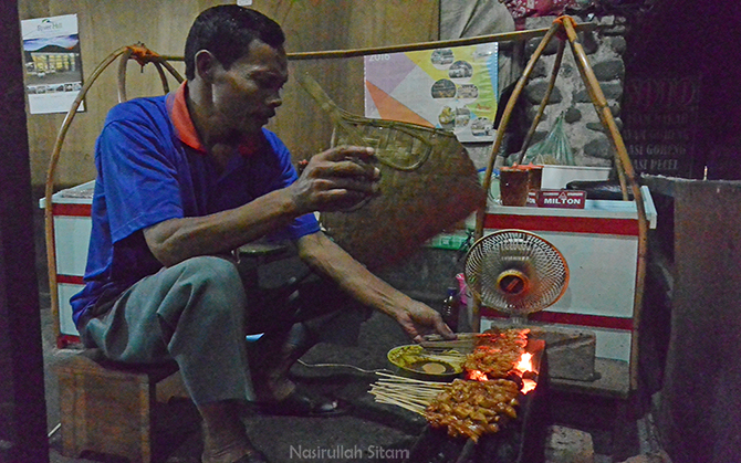 Pak Temon mengipasi sate kelinci yang sedang dibakar