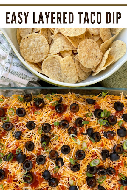Finished layered taco dip with a bowl of tortilla chips.