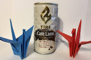 A picture of two folded origami cranes either side of a can of Fire Kirin coffe made using the Miura fold