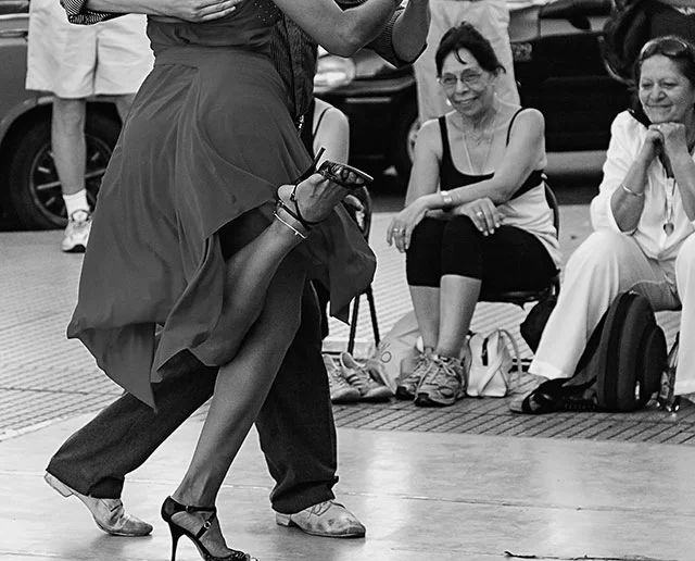 Dos mujeres espectadoras sonrientes ante vaile de pareja de tangos.