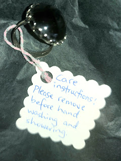 a black and silver cocktail ring with a paper tag attached with care instrucitons