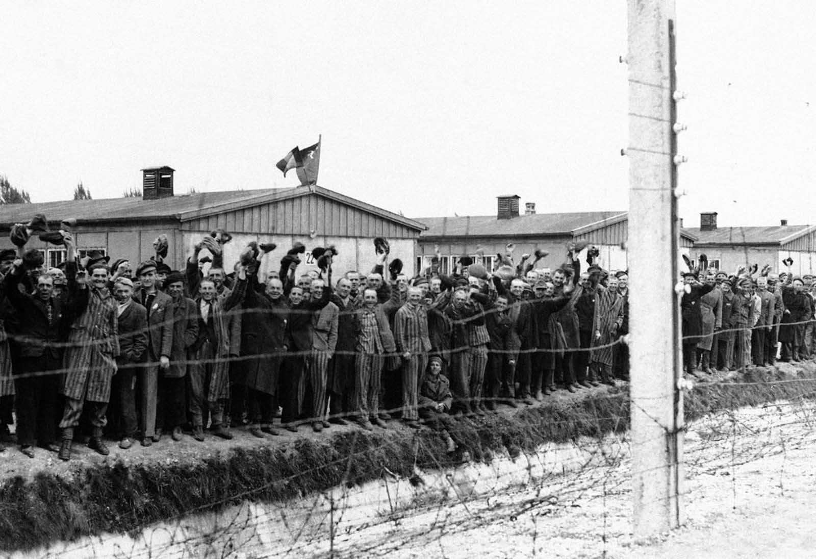 Prisoners at the electric fence of Dachau concentration camp cheer American soldiers in Dachau, Germany in an undated photo. Some of them wear the striped blue and white prison garb. They decorated their huts with flags of all nations which they had made secretly as they heard the guns of the 42nd Rainbow Division getting louder and louder on the approach to Dachau.