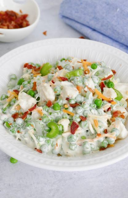 Bacon Ranch Pea Salad in a white bowl with a blue napkin in the background.