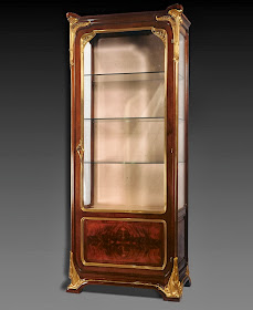 Mahogany display cabinet strictly shaped with the fine, bronze decoration. Framed design is softened by the presence of glowing stylised flowers rolling over the corners, the sides and footboards