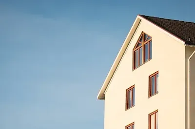 Foto Imagem da lateral de um edifício de alvenaria pintado na cor amarelo claro com janelas em madeira natural, ilustrando texto sobre multa condominial