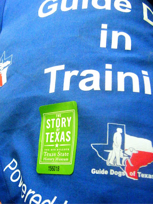 closeup of Alfie's blue jacket with a green sticker on it that says:  The Story of Texas/Texas State History Museum