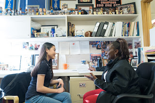 Female adult and female student sit facing each other at a desk in an office.