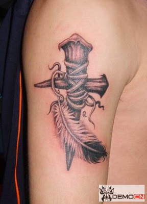 A cross tattoo on the arm with a feather close by.