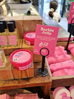 A stack of pink plastic cyldirndial shallow tubs filled with a light pink circular jelly mask with a pink lid and circular label that says barbie jelly jelly mask in white font with a pink rectangular label next to it that says barbie jelly jelly mask in white font on a bright background