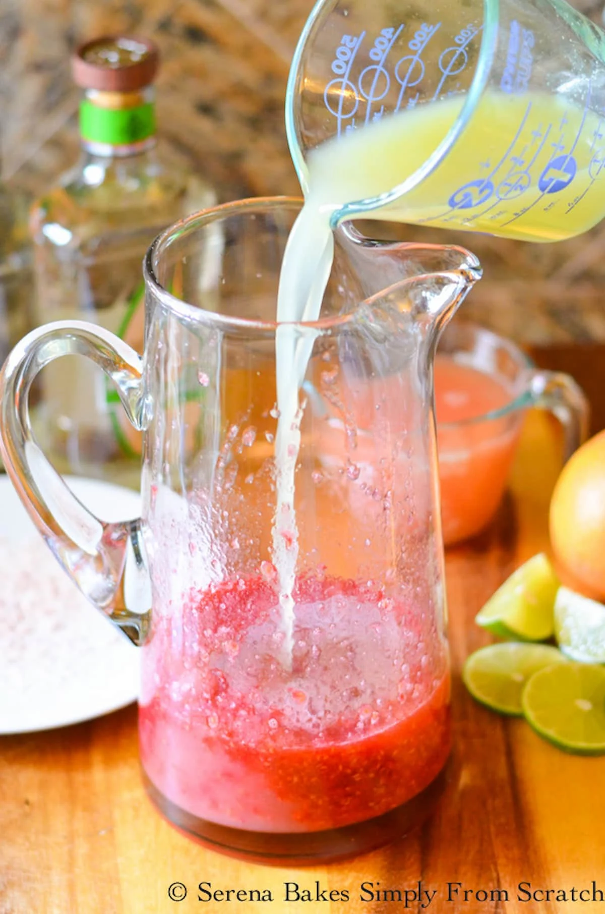 Lime Juice being poured into a glass pitcher with macerated raspberries in it.