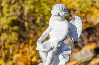 Eros, Greek god of Romantic love. White stone sculpture of a little boy angel on a blurred background of what is clearly a sunny, autumn day.