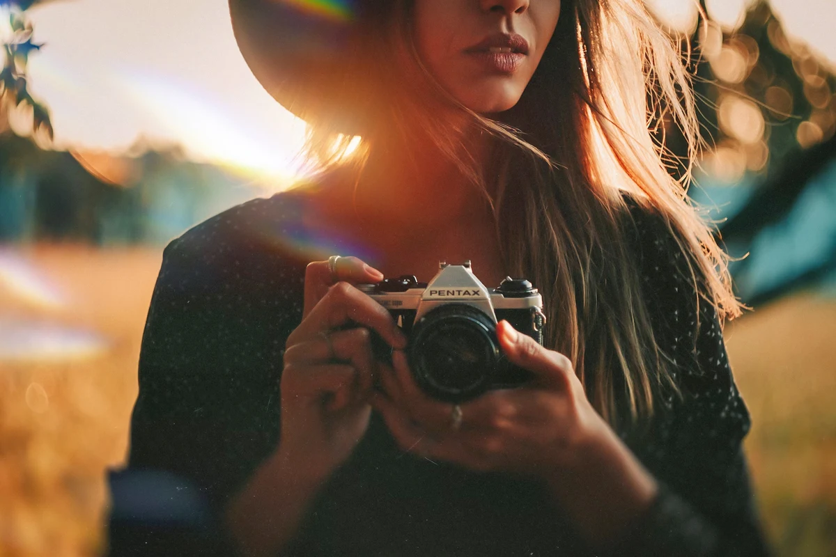 portrait of a beautiful blond woman with a camera in her hand posing in a field