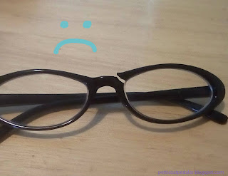 Photo of a pair of black plastic framed glasses with broken frames.  A sad face doodled onto the photo.  