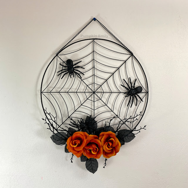 A spider web wreath with orange flowers and spiders.
