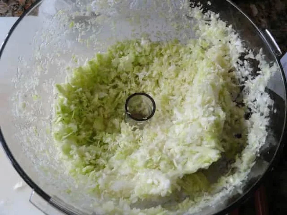 A down shot of shredded cabbage in a food processor.