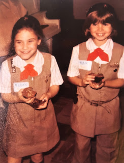 Me, age 7, in a Brownie uniform with number 502 on the shoulder, eating a cupcake, standing next to my red-haired friend Missy, also eating a cupcake.